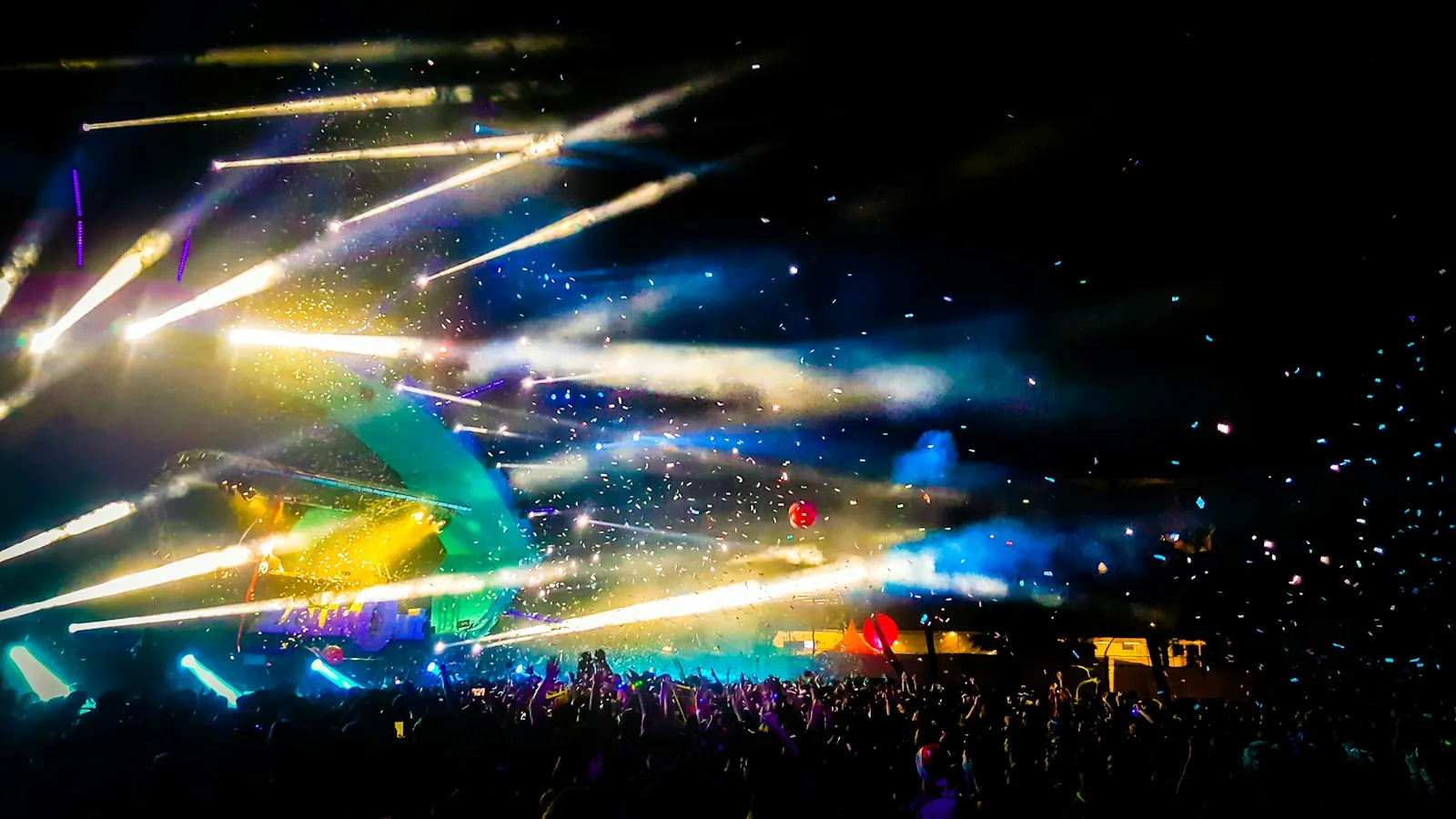 Concert audience beneath sweeping blue and gold stage lights.